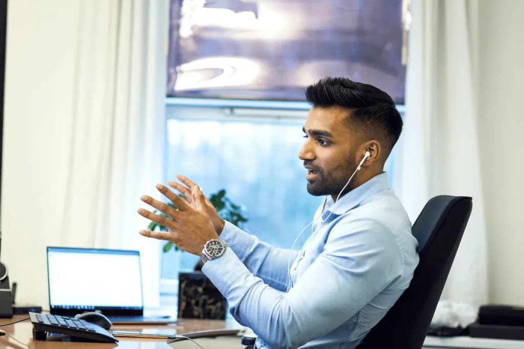 A man wearing earphones engaged in a video call at his desk.