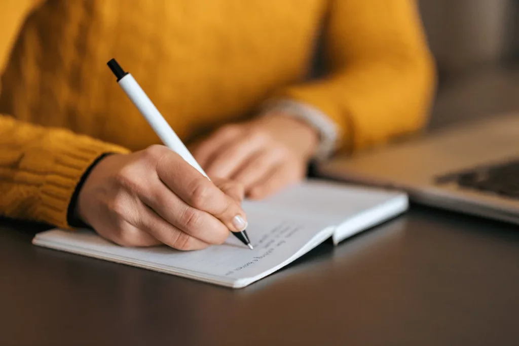 Close-up of hands holding a pen, writing on paper.