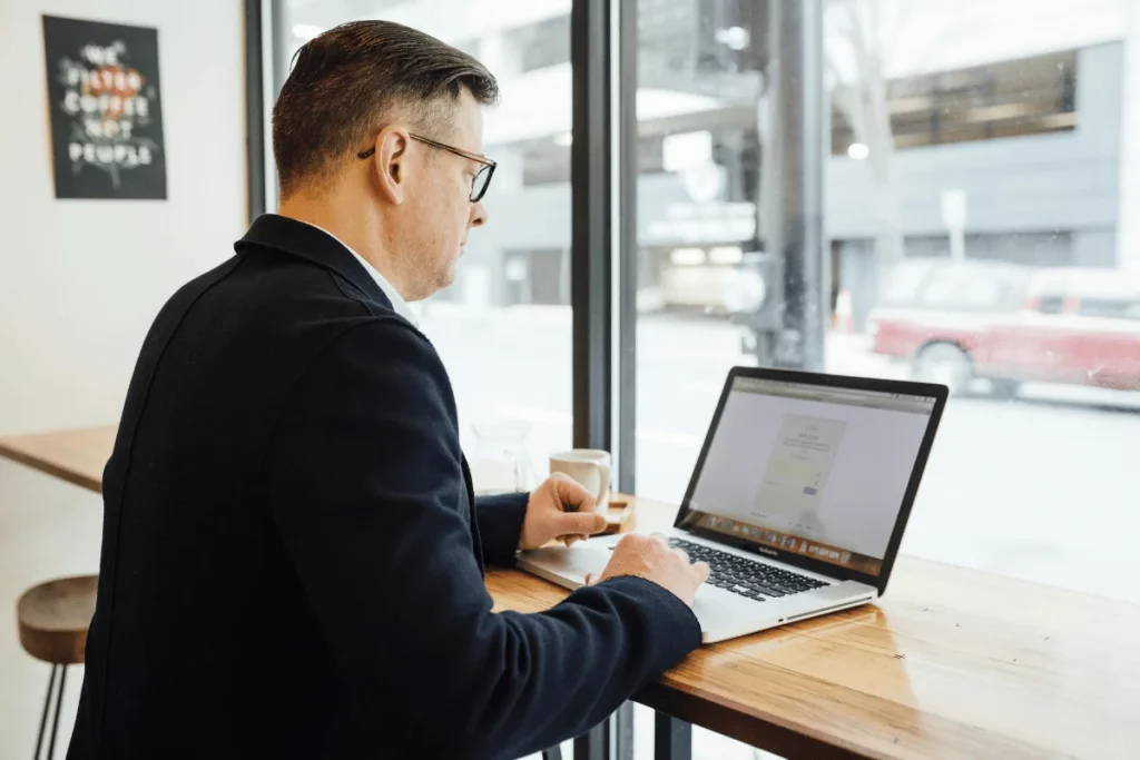 A man working on his laptop while sitting at a café near a window.