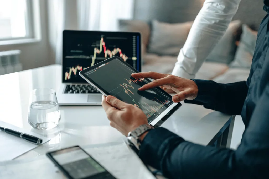 Professional analyzing financial graphs on a tablet with laptop in the background.