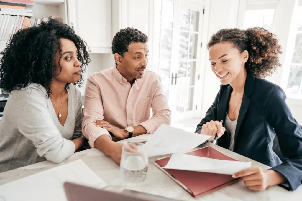 A couple attentively listens to a financial advisor reviewing documents at their home.