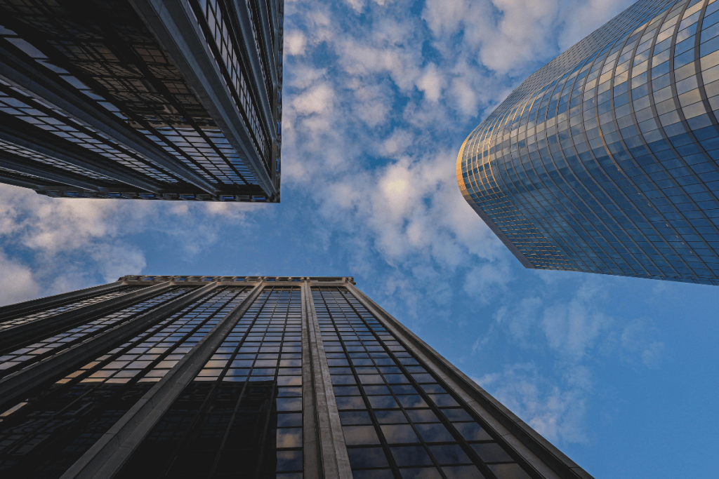 Low-angle view of two towering skyscrapers against a blue sky with white clouds.