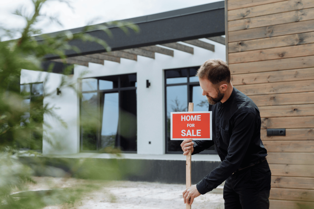 Man setting up a sale sign outside a modern home.