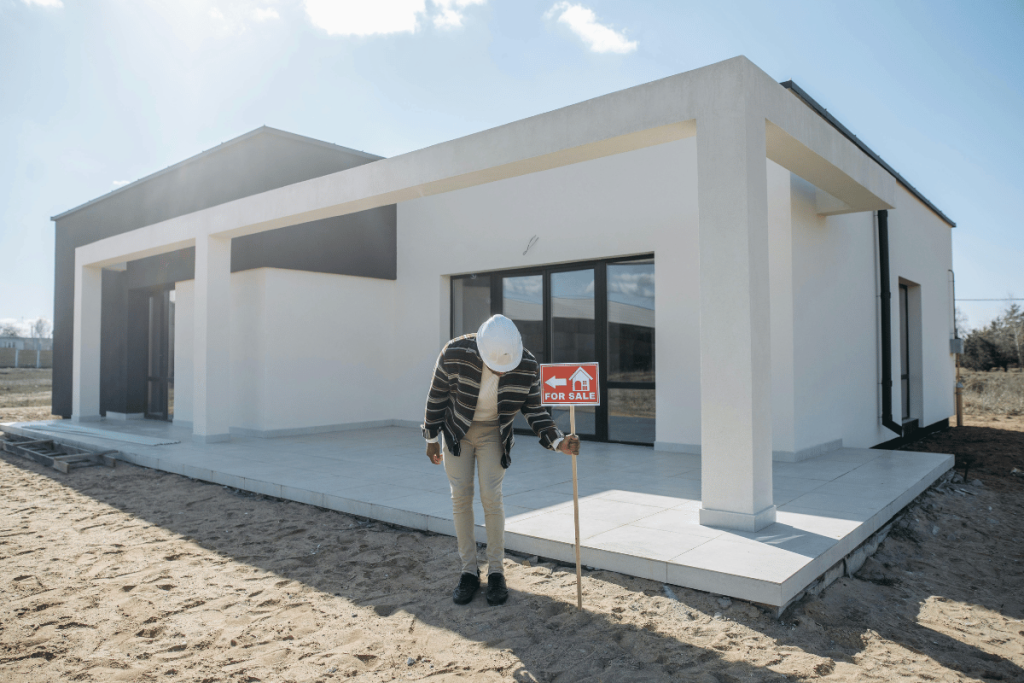 Engineer inspecting a newly built house with a for sale sign.