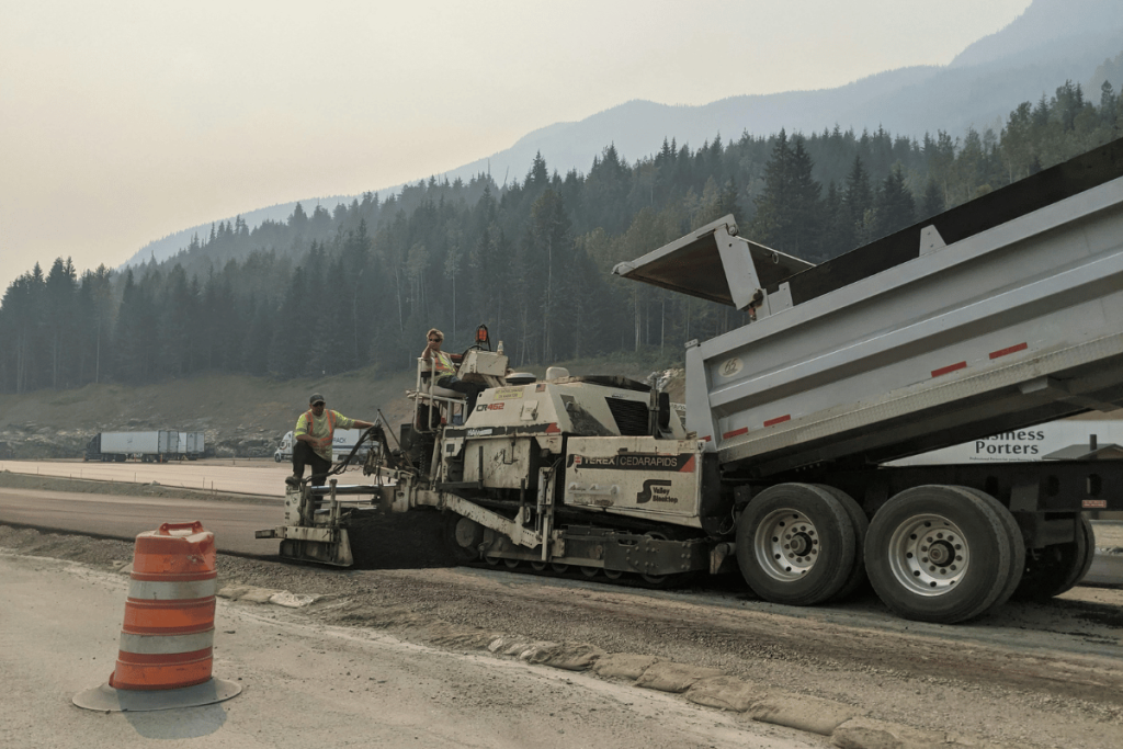 Road construction crew working with paving machinery in a mountainous area.