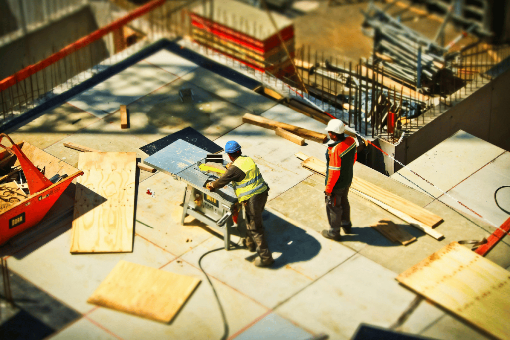 Construction workers cutting wood at a busy construction site with machinery.