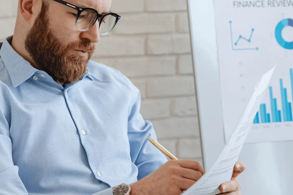 Pensive business analyst examining a report in front of financial statistics.