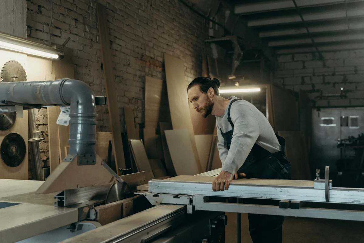 Carpenter operating a table saw while cutting wood in workshop.