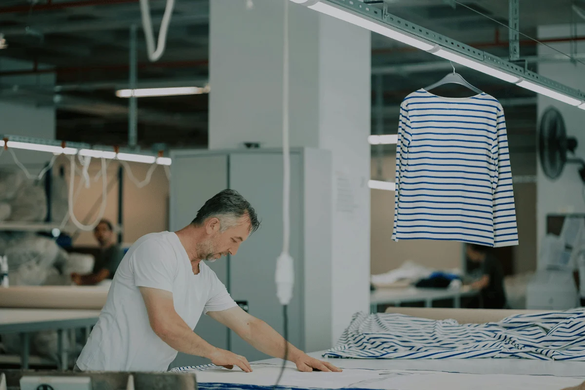 Worker in textile factory cutting fabric for striped shirt production.
