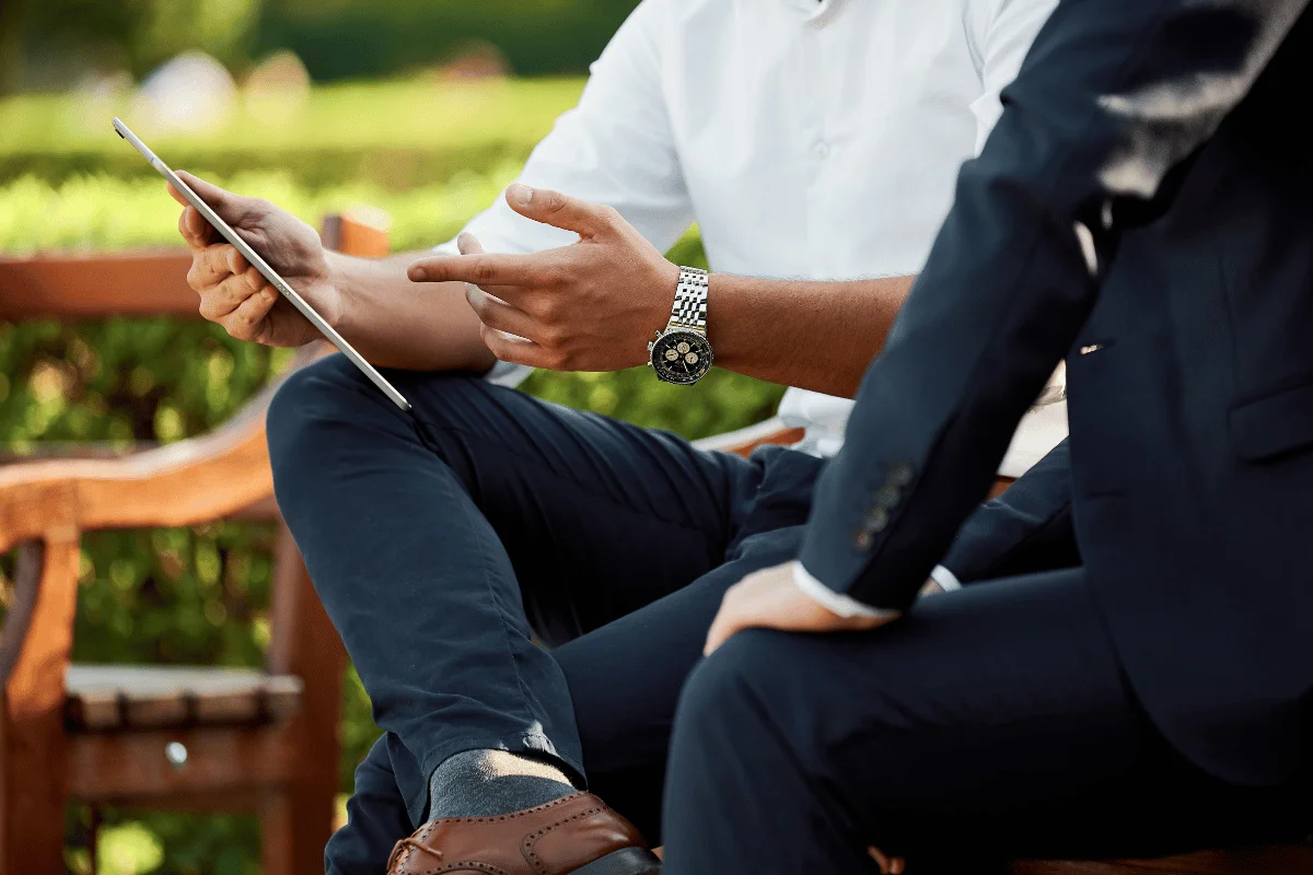 Two men in professional attire discussing work on a tablet.