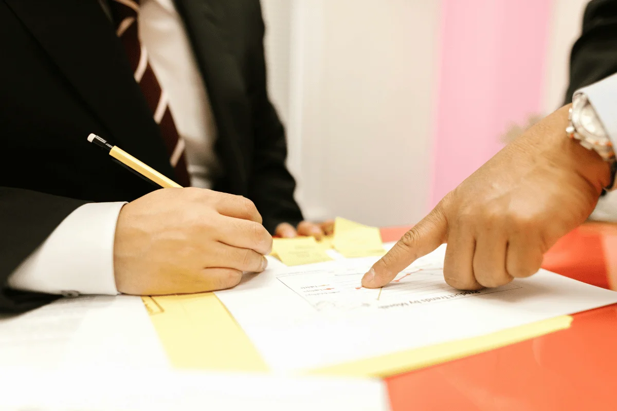 Businessman signing a contract while another person points to a section.
