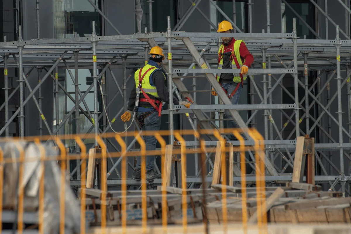Workers in safety gear assembling scaffolding on a construction site.