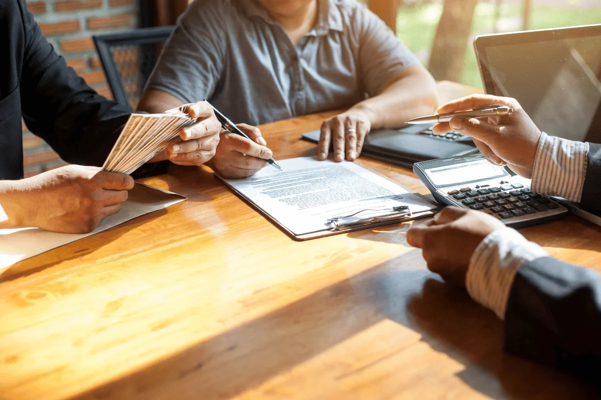 A group of individuals finalizing a financial agreement with calculators and legal paperwork.