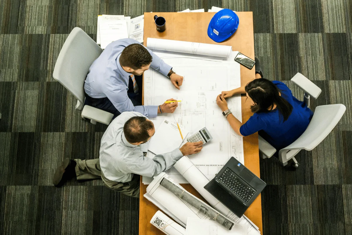 Three professionals reviewing architectural plans together at a conference table.