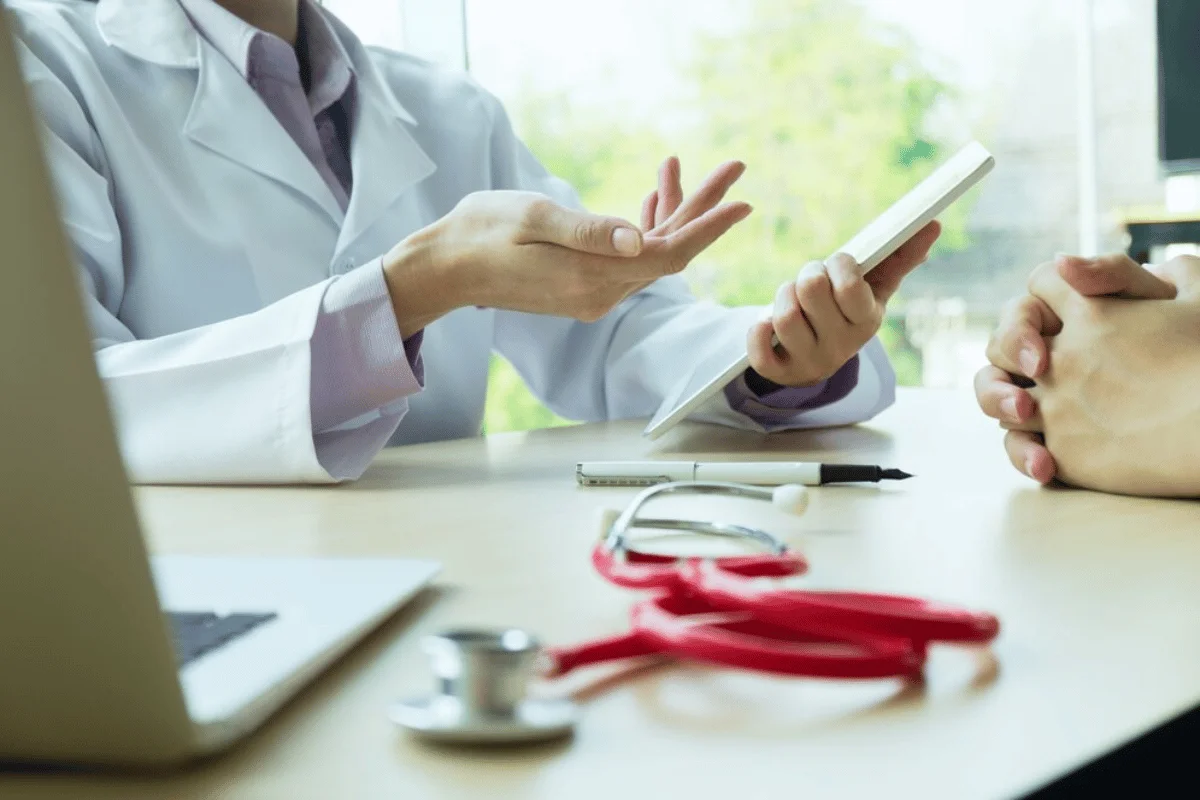 A doctor showing a tablet to a patient while discussing medical information, with a stethoscope on the table.