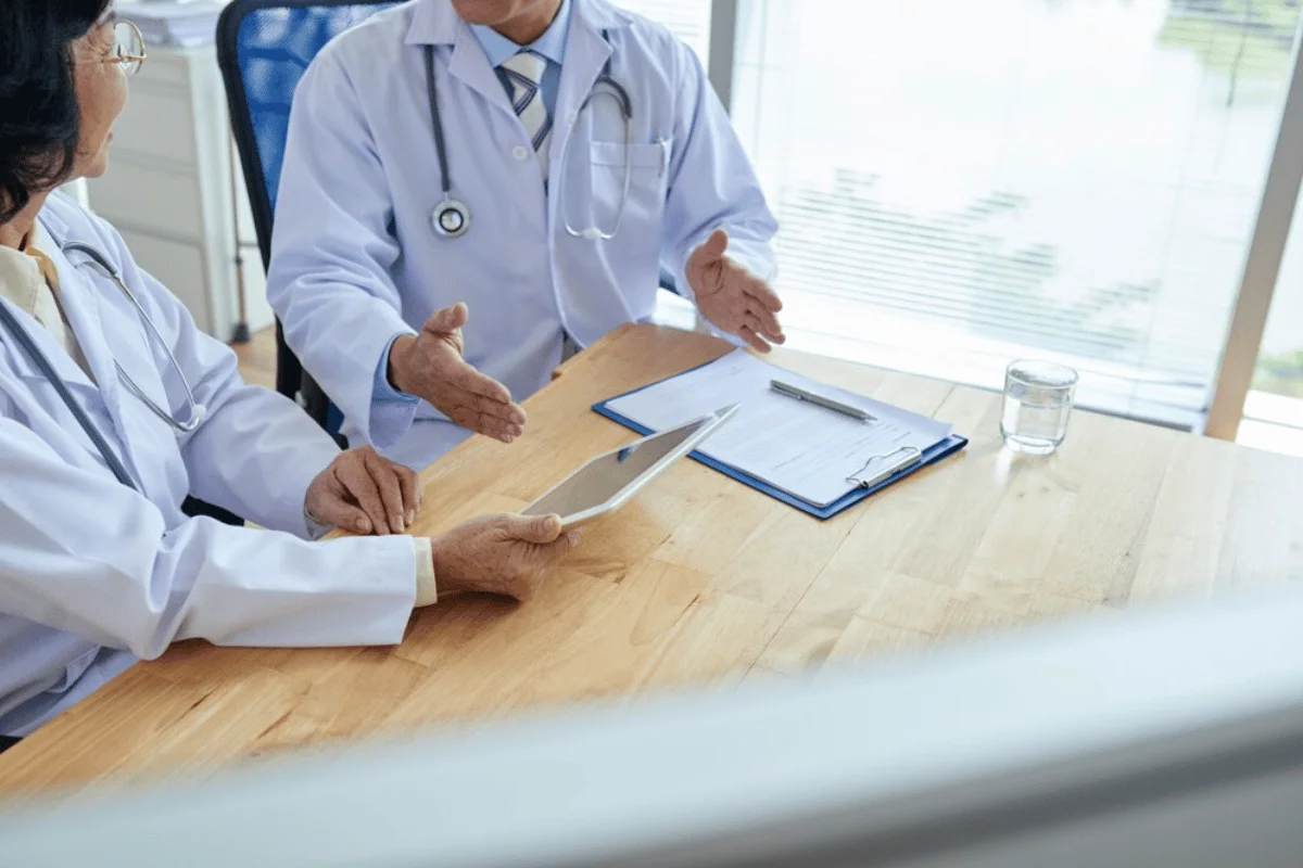 Two doctors discussing a medical case while holding an iPad and sitting at a desk.