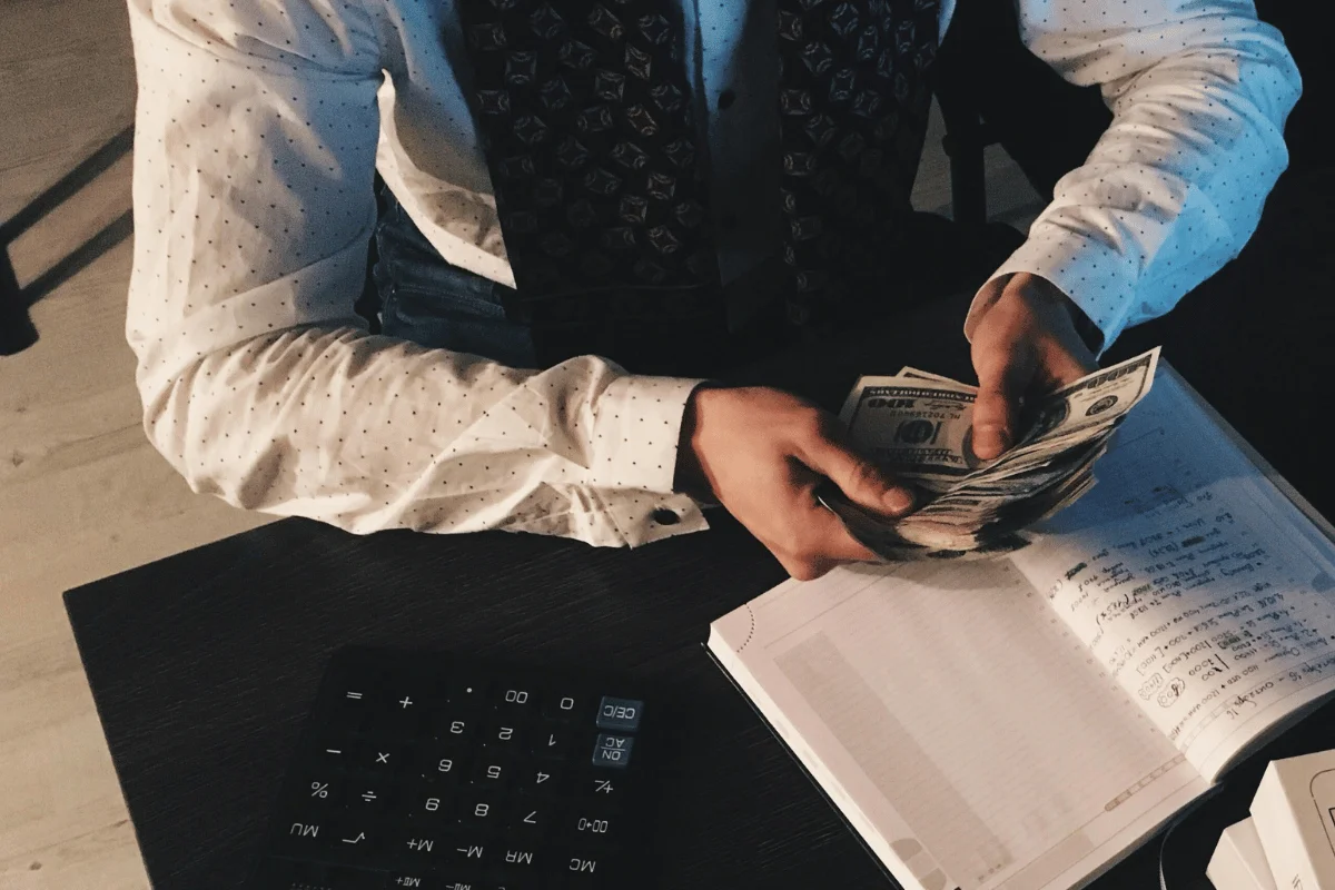 Person organizing cash and making notes with a calculator on the desk.