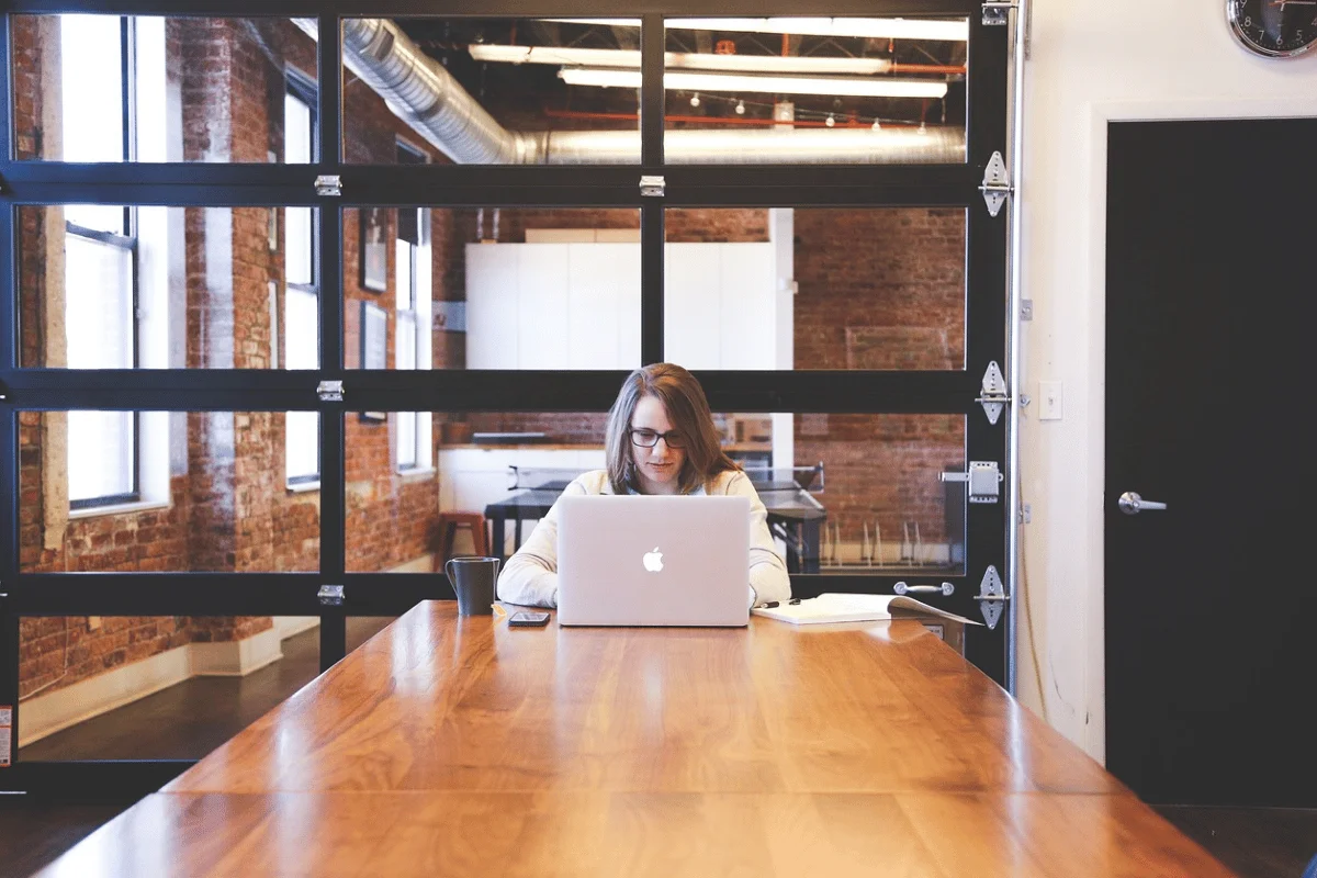 Office scene with a focused employee on a MacBook at a polished wooden table.
