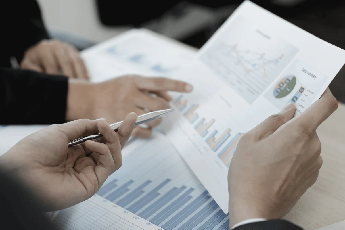 Professionals pointing at financial documents with charts and graphs for analysis.