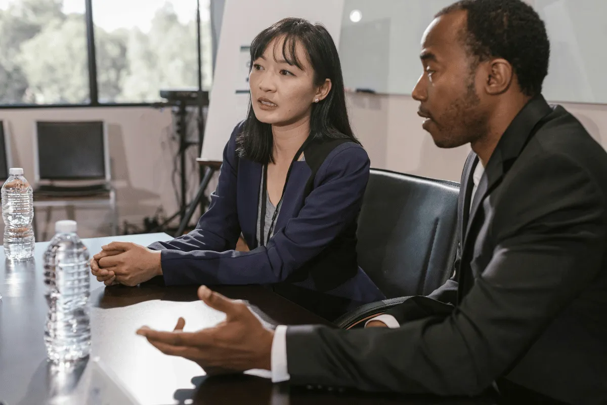 A woman attentively listens while her colleague speaks in a formal meeting.