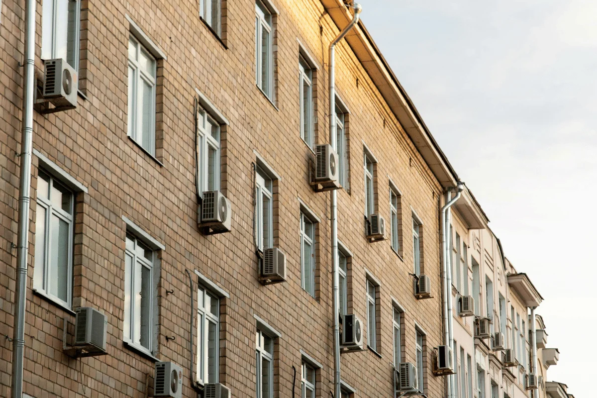 Brick apartment building with multiple windows, each featuring installed air conditioning units.