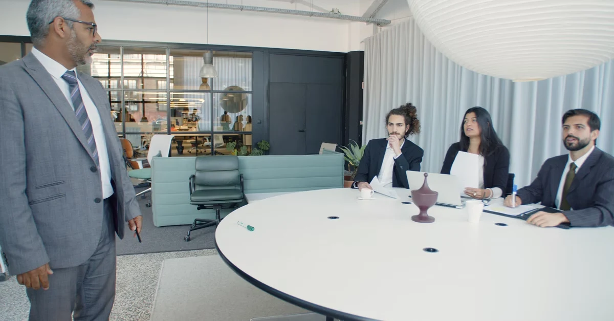 Senior executive presenting to potential investors at boardroom table during SaaS company acquisition discussion.