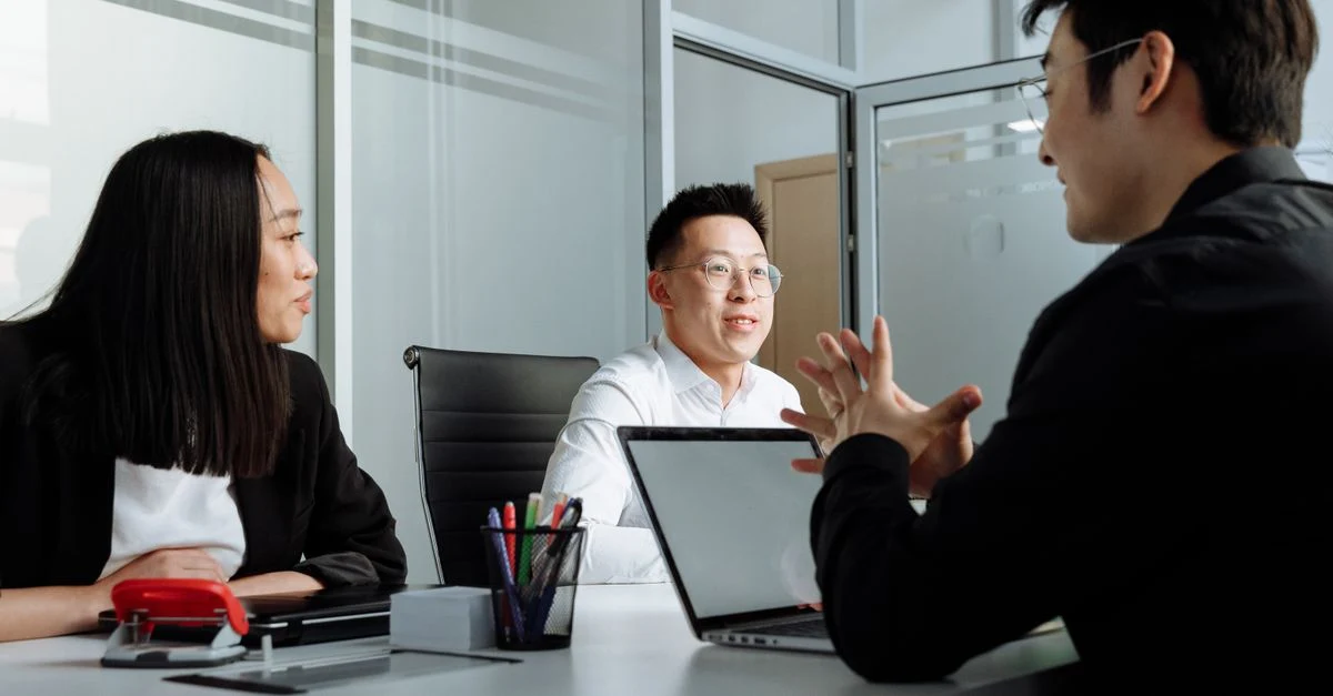 Three professionals reviewing documents during saas M&A due diligence meeting in modern office conference room.