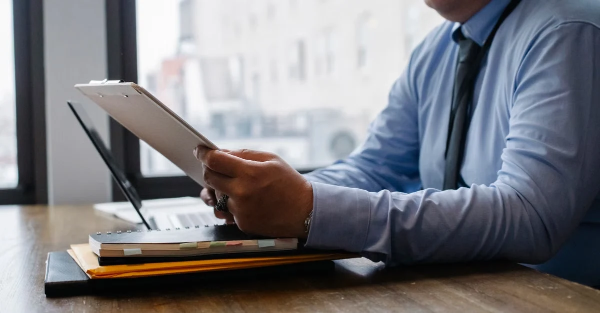 Businessman reviewing saas ma report on tablet at office desk with city skyline view.
