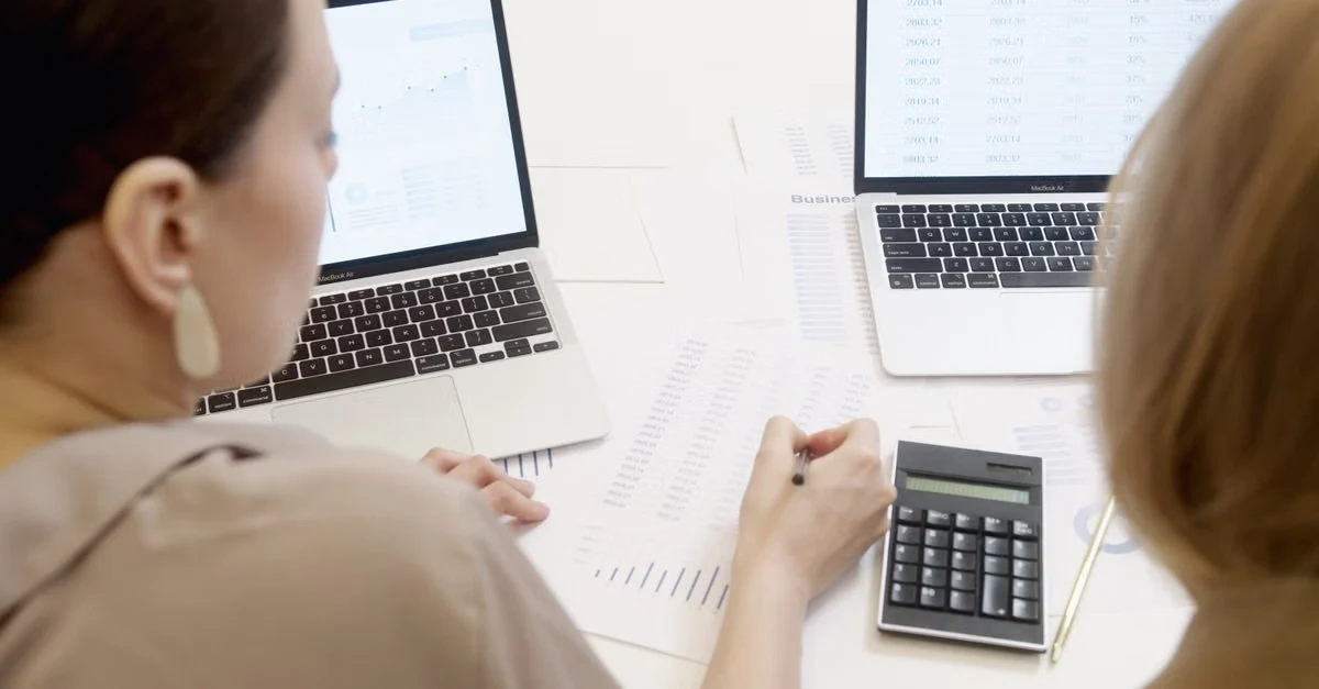 Two professionals reviewing SaaS M&A report documents with laptops and calculator at desk.