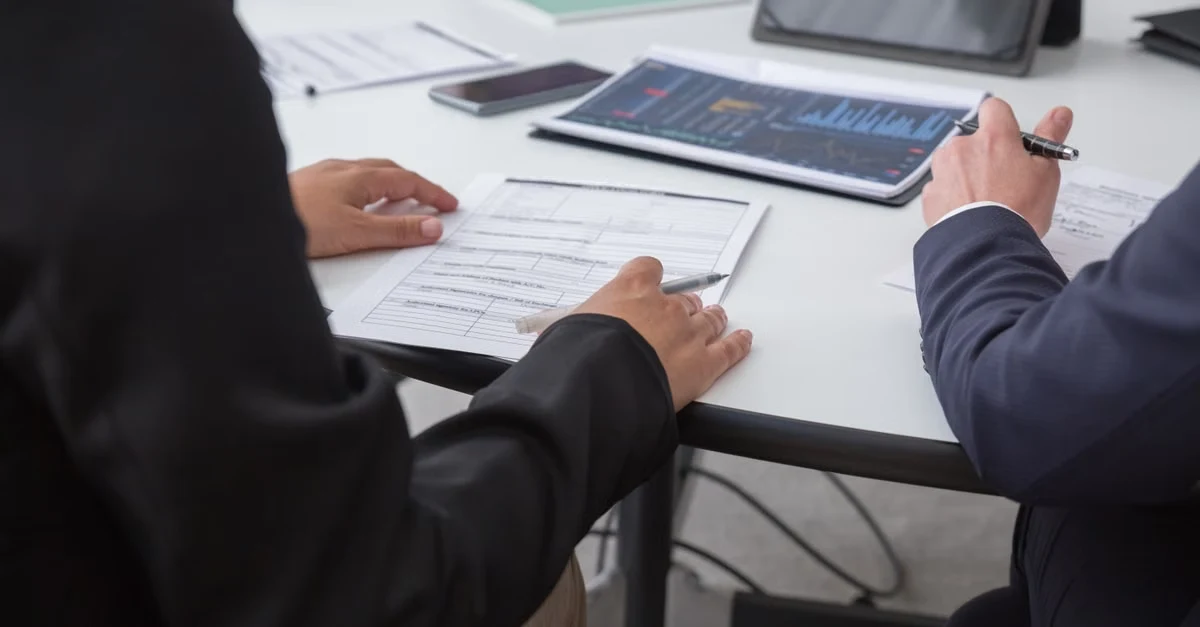 Two professionals reviewing marketing agency valuation multiples and financial documents at white desk with tablet and charts.