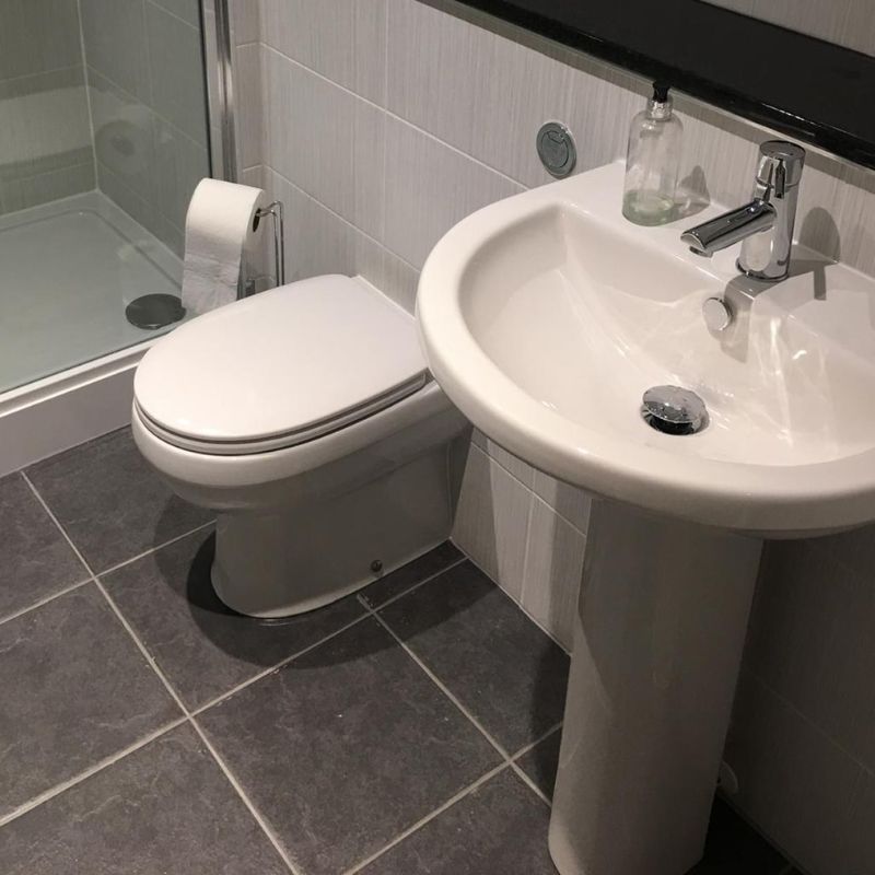 Modern bathroom corner with a closed white toilet, a pedestal sink with a faucet and soap dispenser, and a glass-enclosed shower.