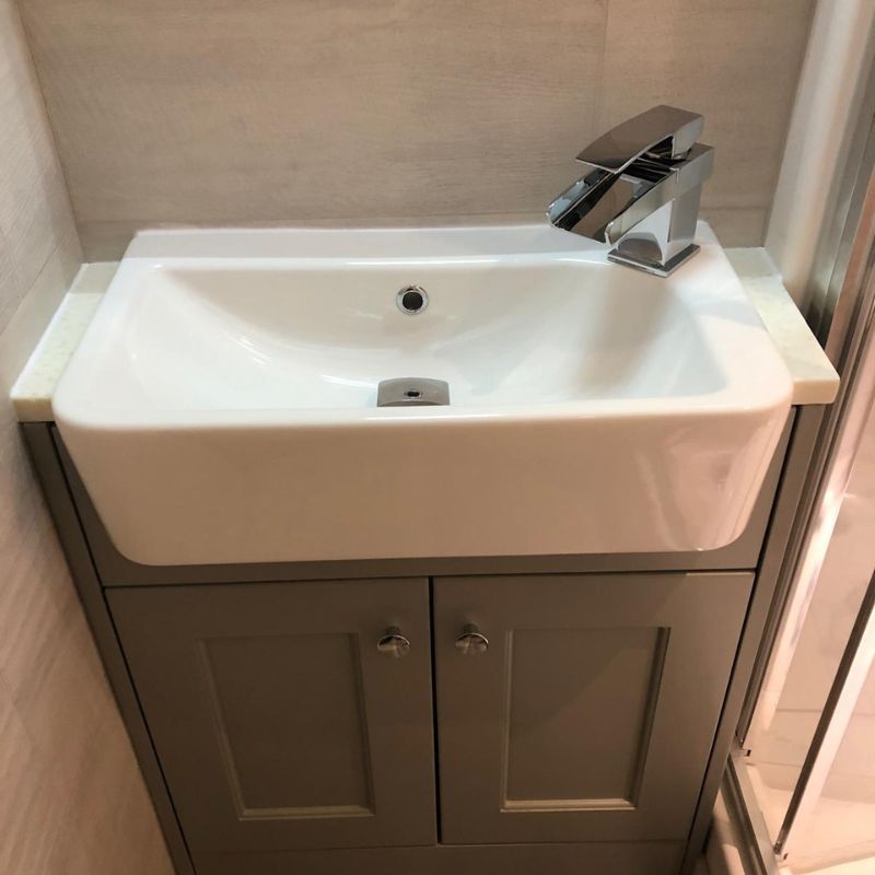 White rectangular bathroom sink with a modern chrome faucet mounted on a gray cabinet with two doors below.