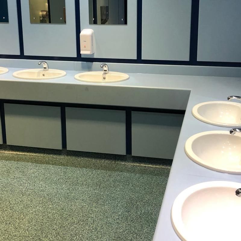 Modern public bathroom sink area with five white sinks, three mirrors, and a wall-mounted soap dispenser.