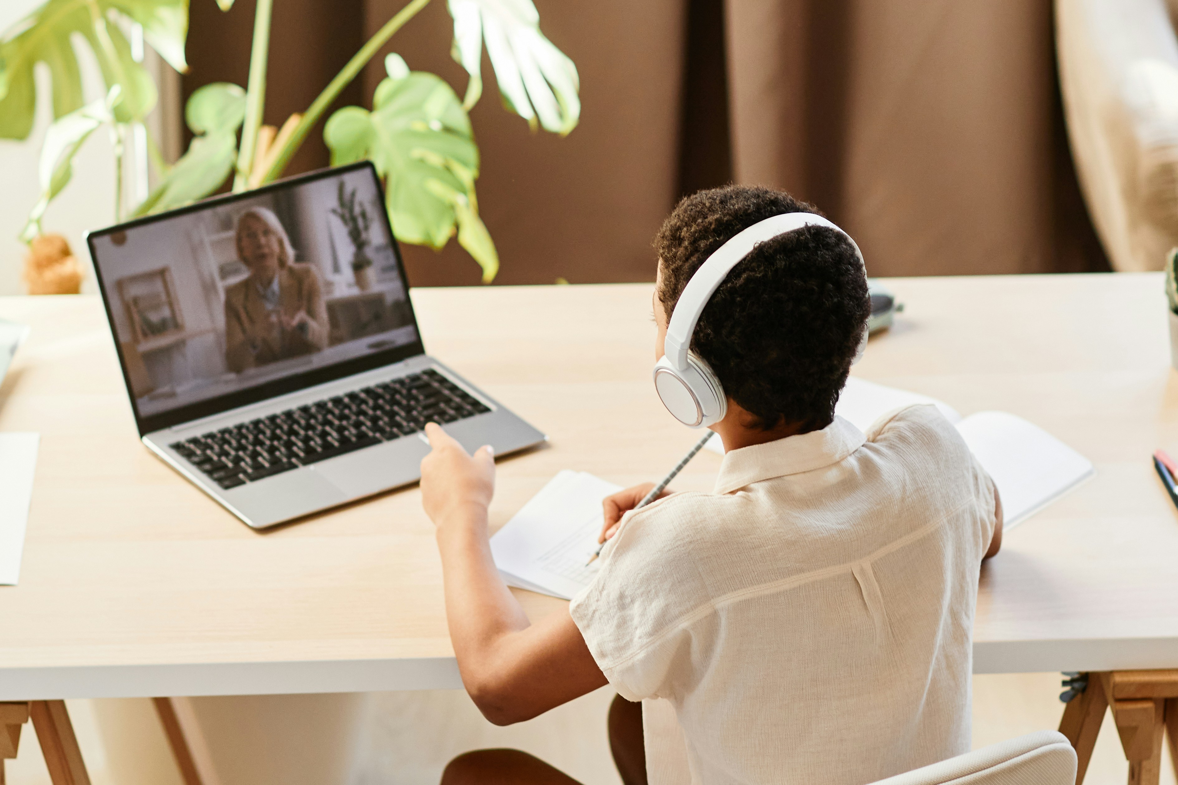 Student wearing headphones and taking notes during an online lesson, illustrating online teaching tips for keeping learners engaged in a virtual classroom.