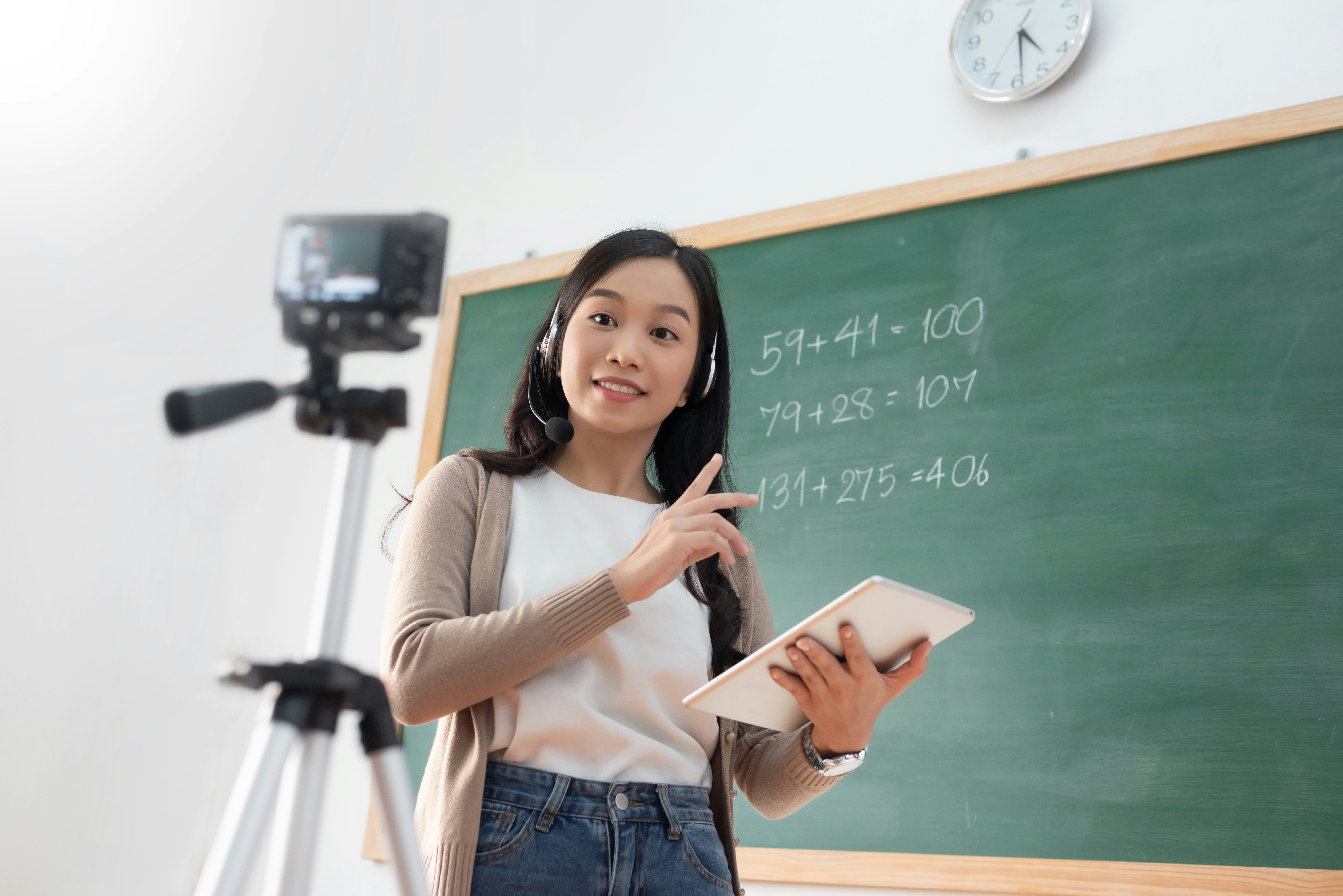 Teacher recording a lesson in front of a blackboard while learning how to start an online tutoring business from home.