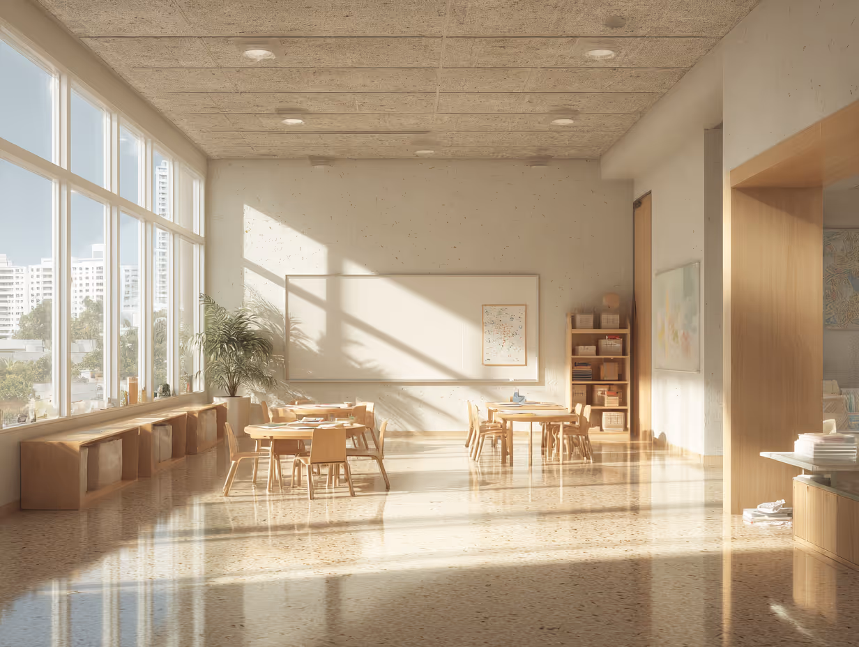 Sunlit classroom with large windows, small wooden tables and chairs, a whiteboard, and shelves with books and supplies.