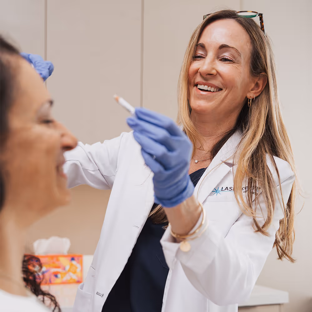 A woman is at her appointment for Dysport injections at Laser Center of Marin and smiling next to a provider holding a white pencil