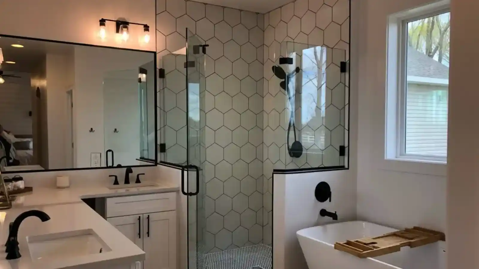 Modern bathroom design showcasing a double vanity with matte black hardware, a glass-enclosed shower with white hexagon tile, and a freestanding soaking tub.