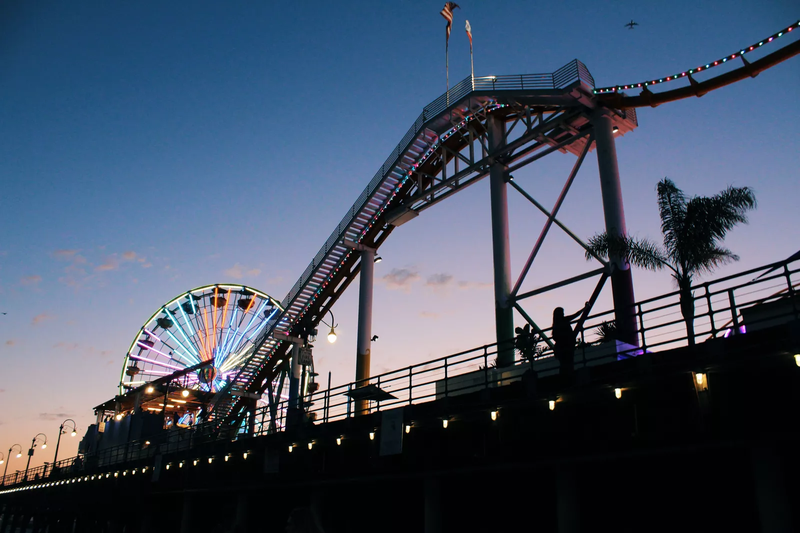 Aerial view of a crowded sandy beach with turquoise ocean waves, rocky coastline, and houses on a hillside in a coastal town.