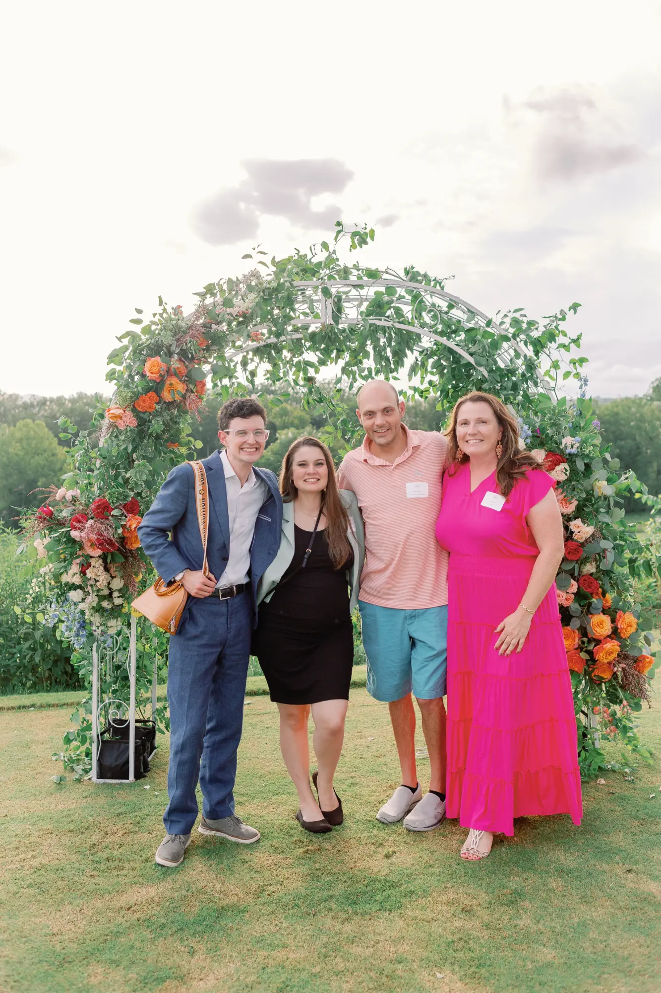 Four people standing together and smiling in front of a flower-decorated arch.