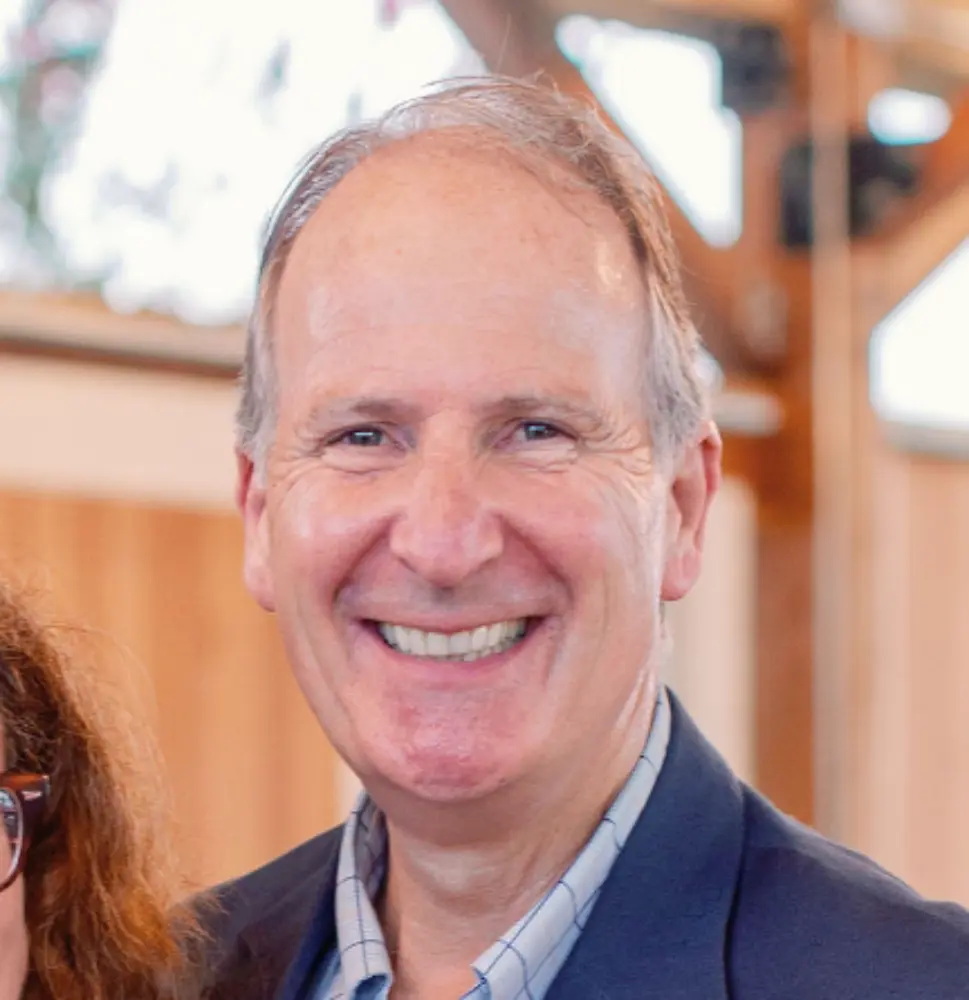 Smiling middle-aged man with light hair wearing a navy blazer and checkered shirt.