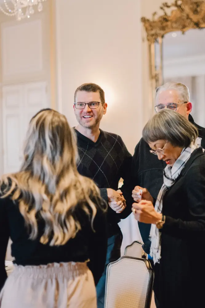 Group of four adults socializing indoors, with two men smiling and two women engaged in conversation.