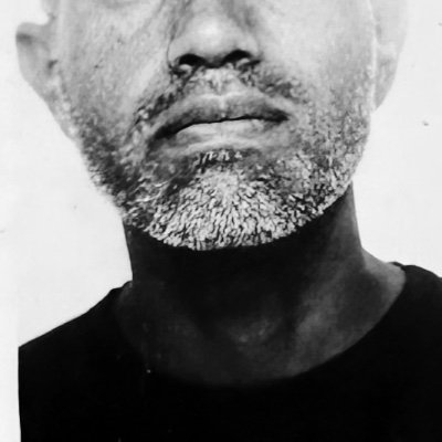 Black and white close-up of the lower face and neck of a man with a short salt-and-pepper beard and mustache wearing a dark shirt.
