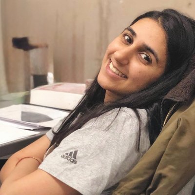 Portrait of a young man with short dark hair, beard, black-framed glasses, and a black collared shirt against a white background.