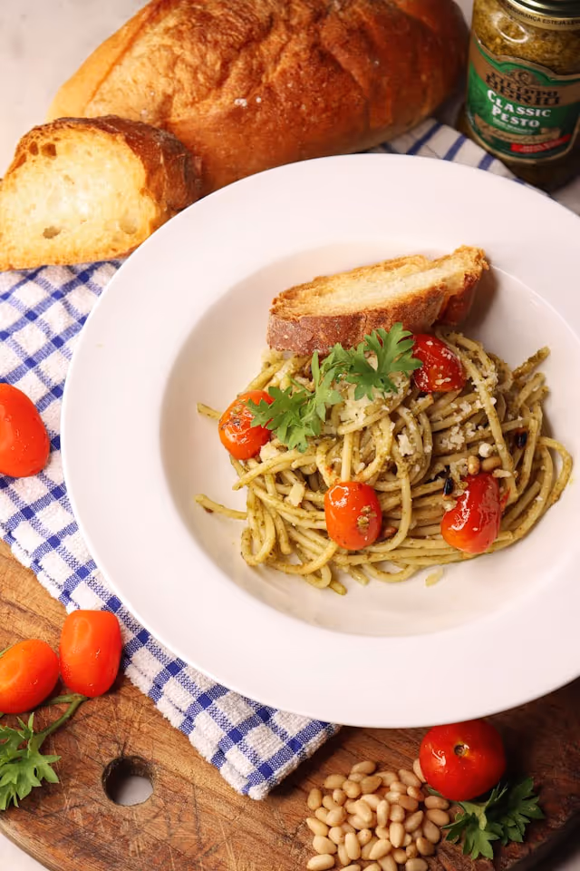 A serving of pasta mixed with green pesto and cherry tomatoes.
