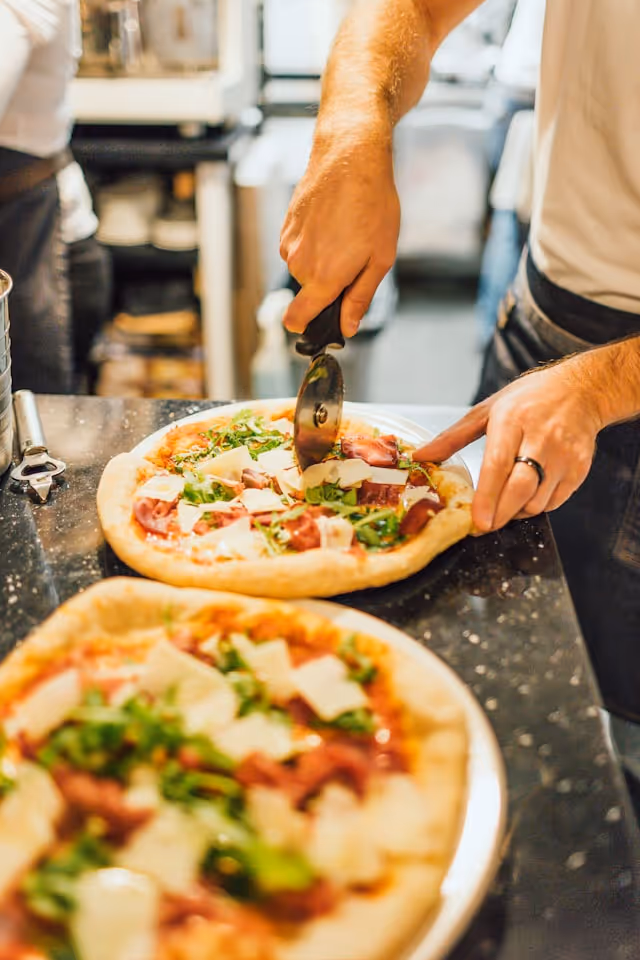 A man using a pizza cutter to slice a pizza on a table.
