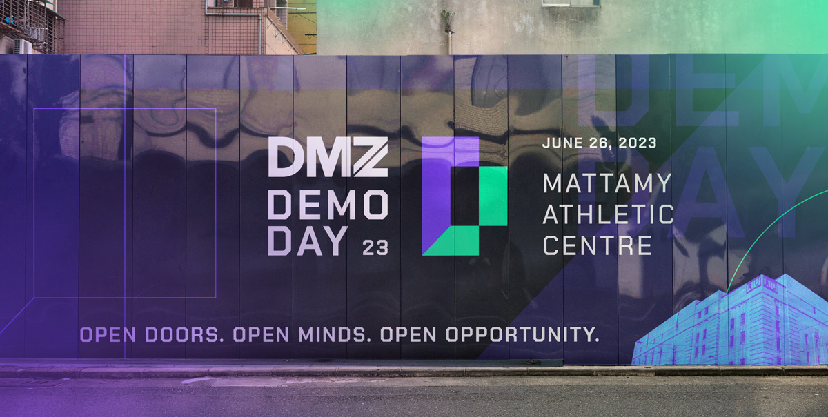 A street scene showing printed promotion for DMZ Demo Day on a construction barrier.