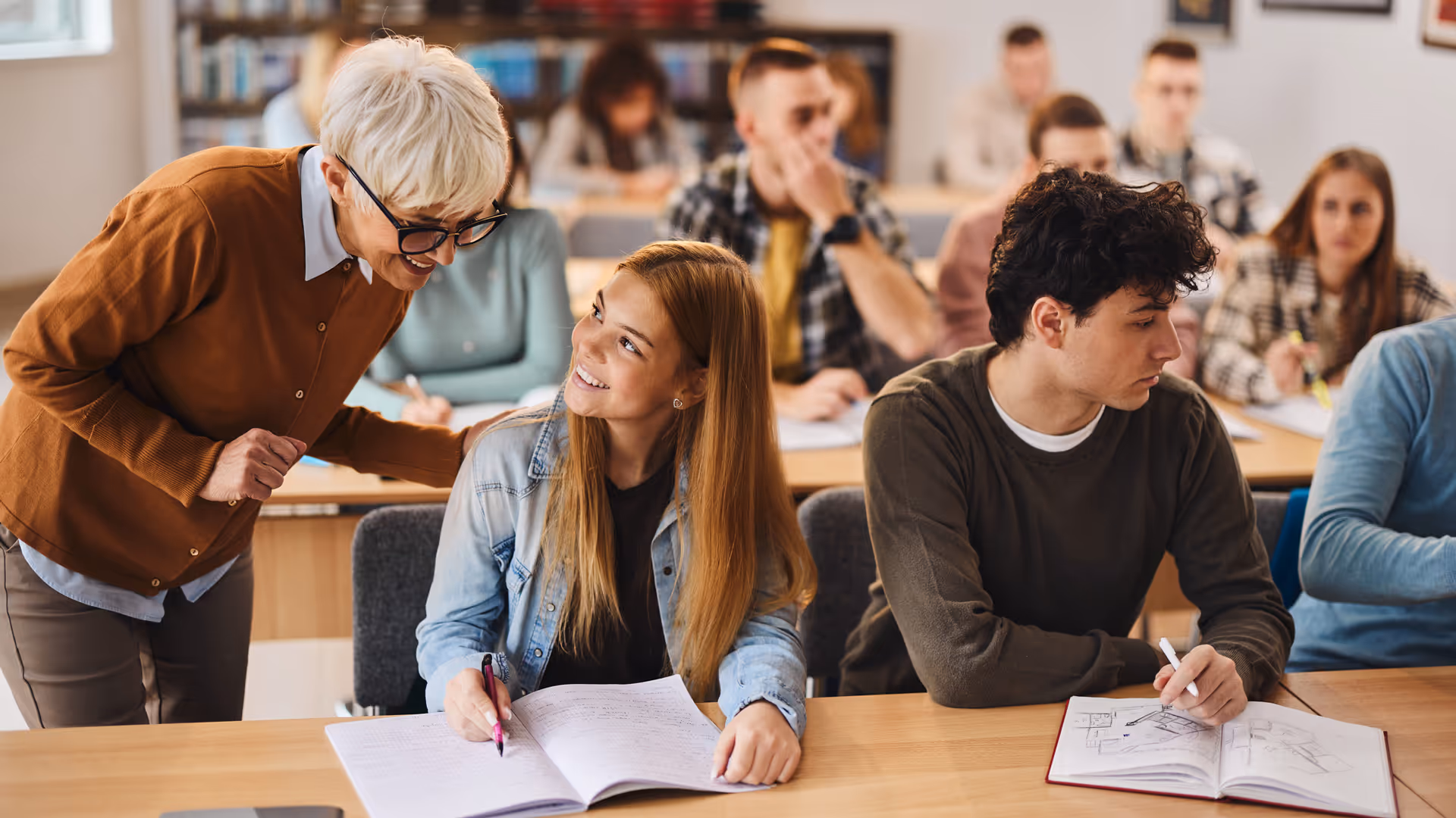 Happy senior professor assisting her student on a class in the classroom