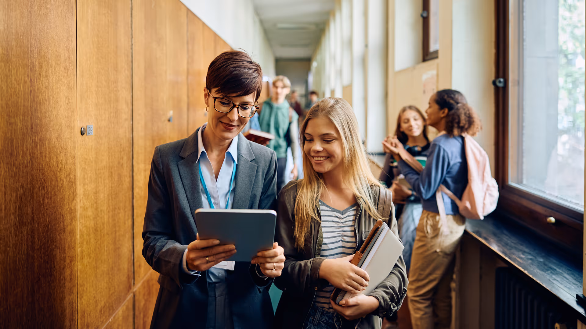 Happy high school teacher and her student using touchpad in hallway