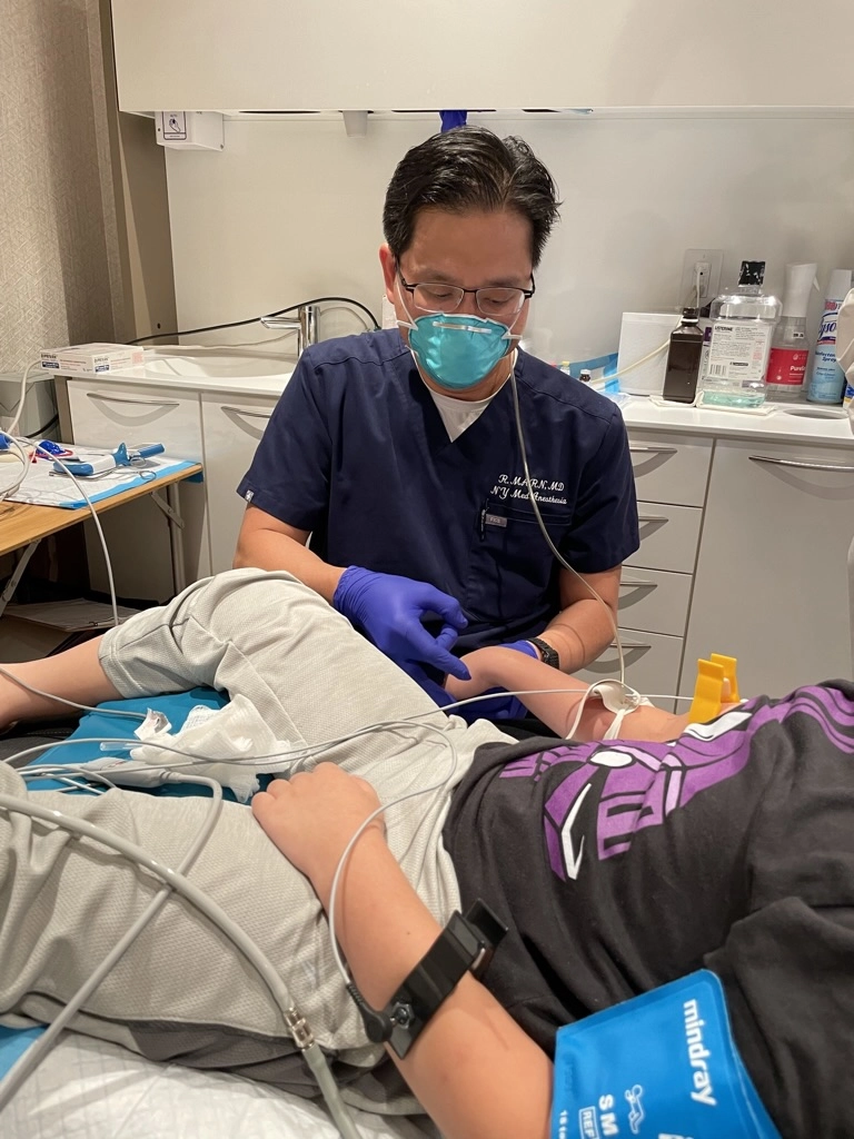 Dr. Marn wearing gloves and a mask administers treatment to a young patient lying on an exam chair.